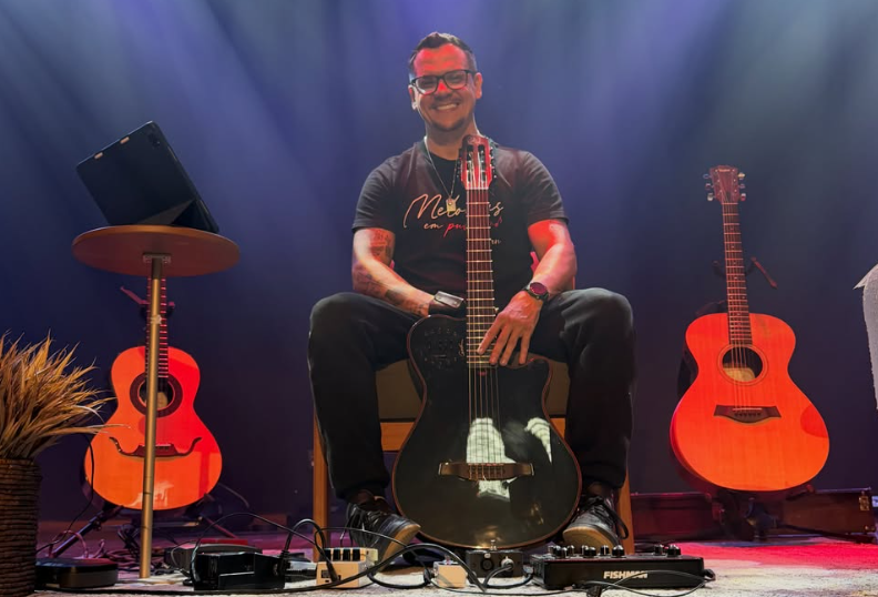 Zaidan sentado com violão, instrumentos e pedais no palco